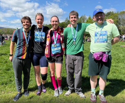 Five members of the relay team on the grass after the race, wearing their race bibs and finisher medals